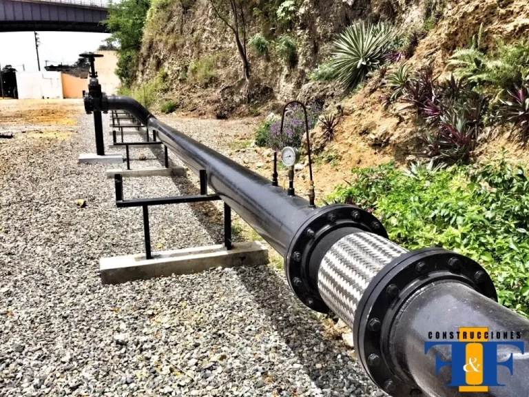 Sistema de tubería industrial con junta flexible y manómetro, instalado en entorno natural.